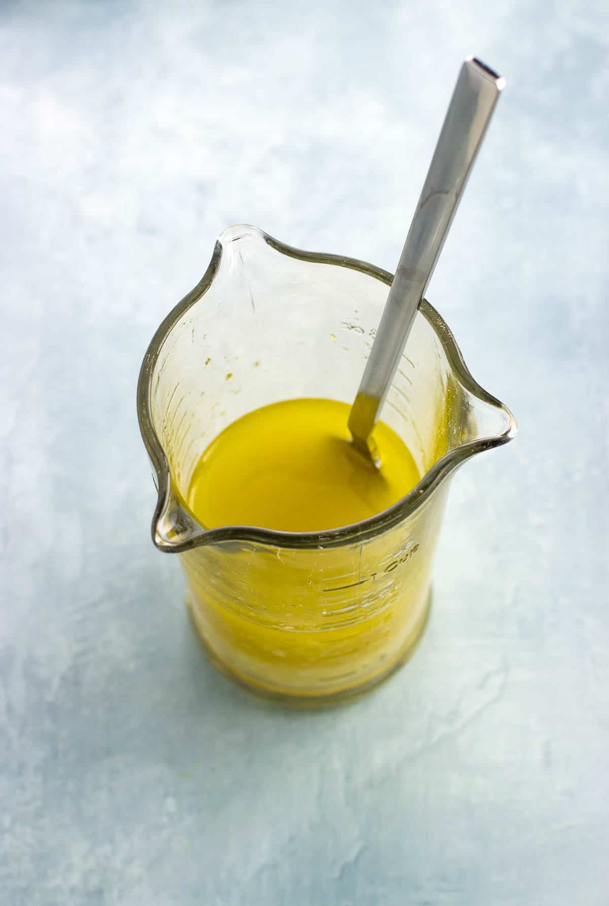 Quinoa salad dressing combined in a glass measuring cup with a fork.