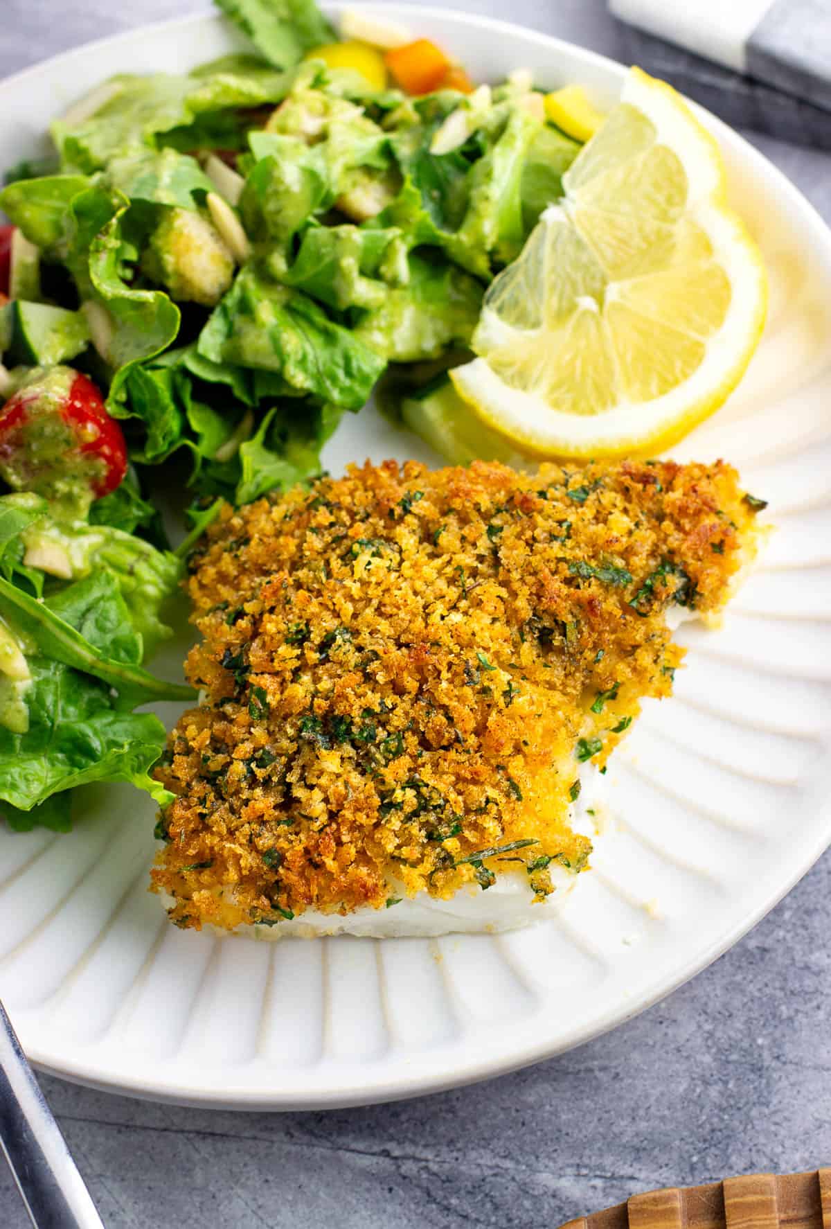 A whole cod fillet on a plate topped with a crispy baked panko crust.