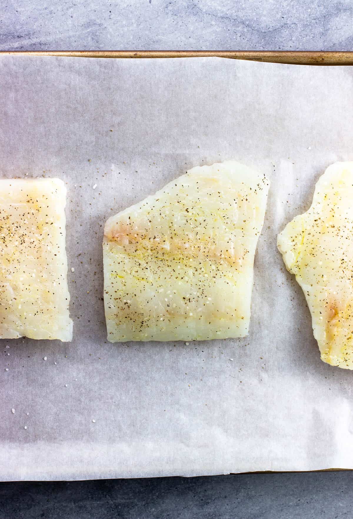 Raw cod fillets brushed with olive oil and seasoned with salt and pepper.