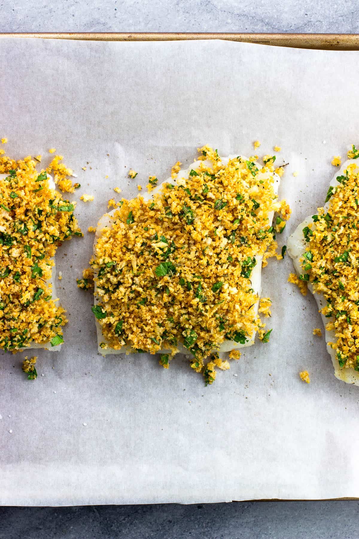 The panko crust topping added to the cod fillets on a sheet pan.