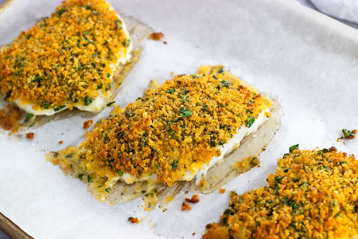 Three baked cod fillets on a parchment-lined baking sheet.