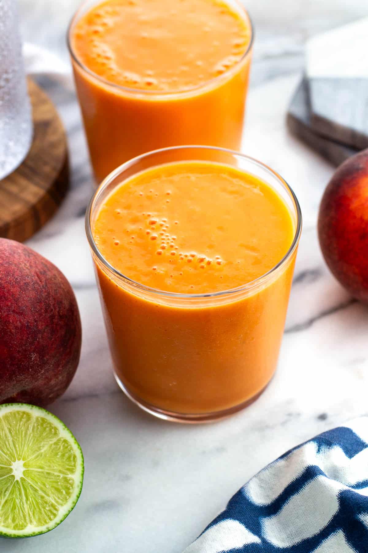 Two peach mango smoothies surrounded by fresh fruit.