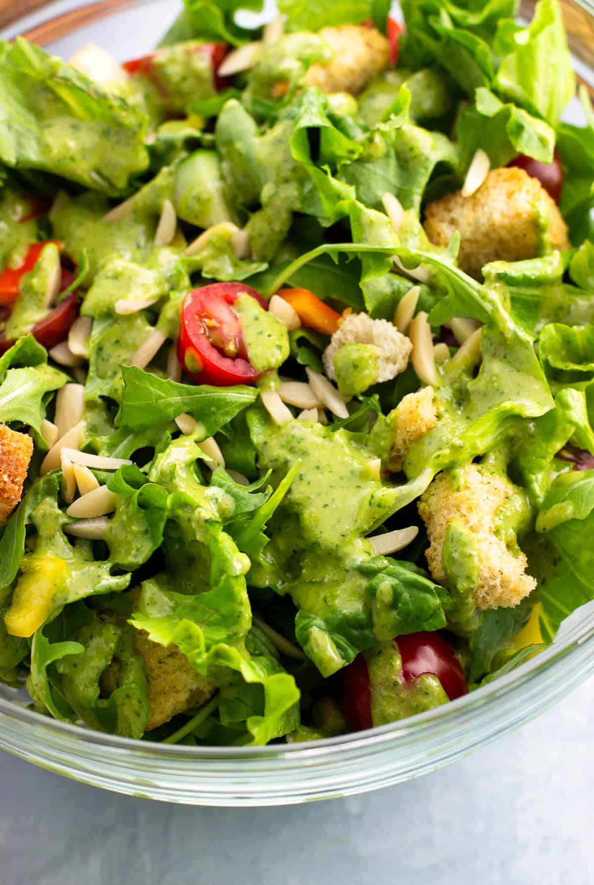 Thick and creamy pesto salad dressing poured over a big bowl of salad greens.