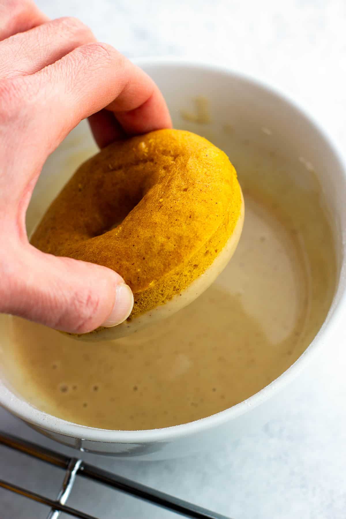 A hand dipping a pumpkin donut into the glaze.