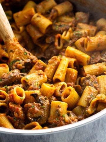 Pasta alla boscaiola in a saucepan with a wooden spoon.