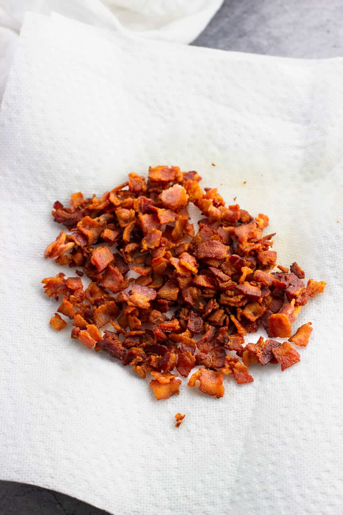 Cooked bacon crumbles on paper towels.
