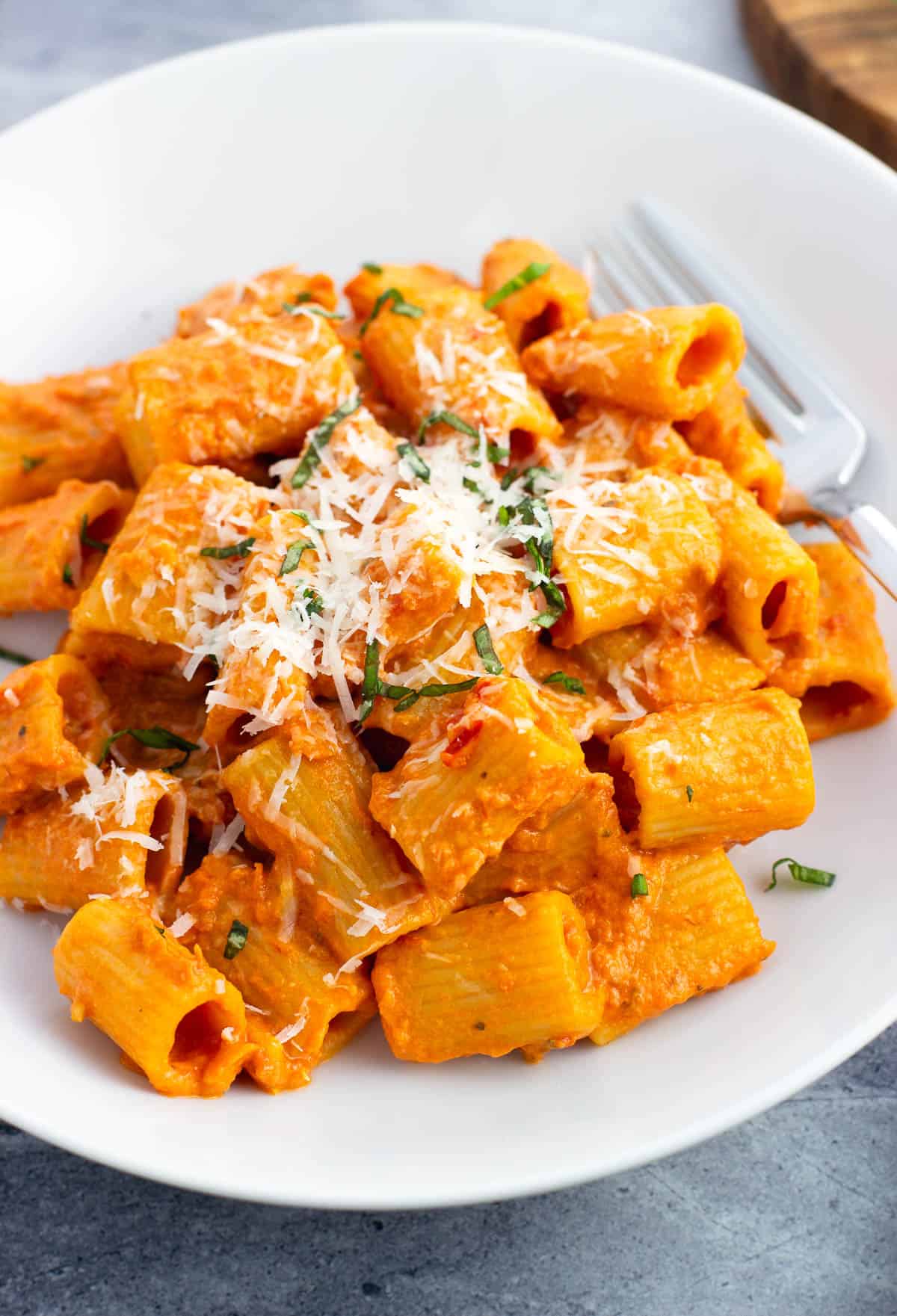 A plate of spicy rigatoni garnished with grated cheese and basil.