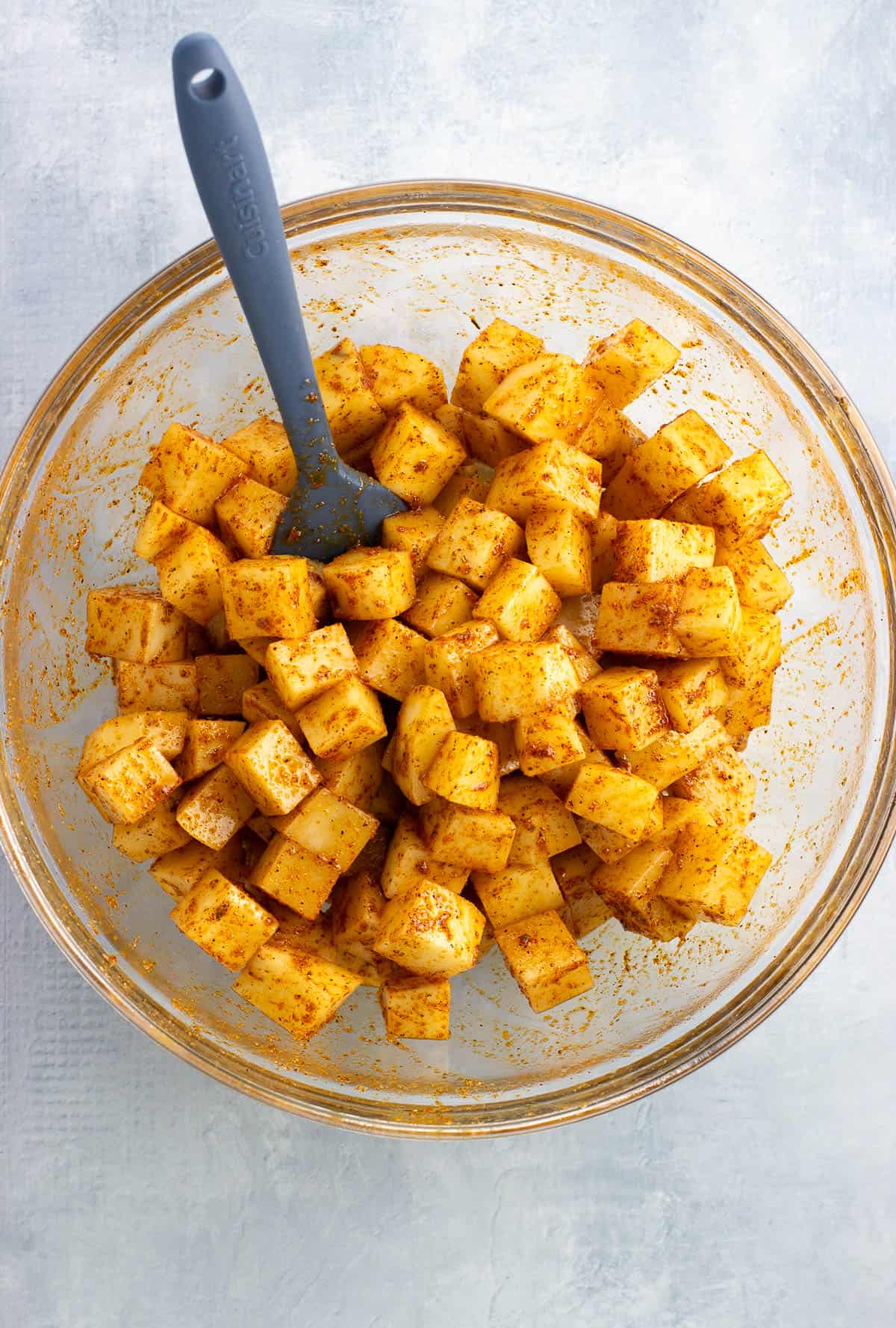 Potato cubes, oil, and seasoning stirred together in a bowl.