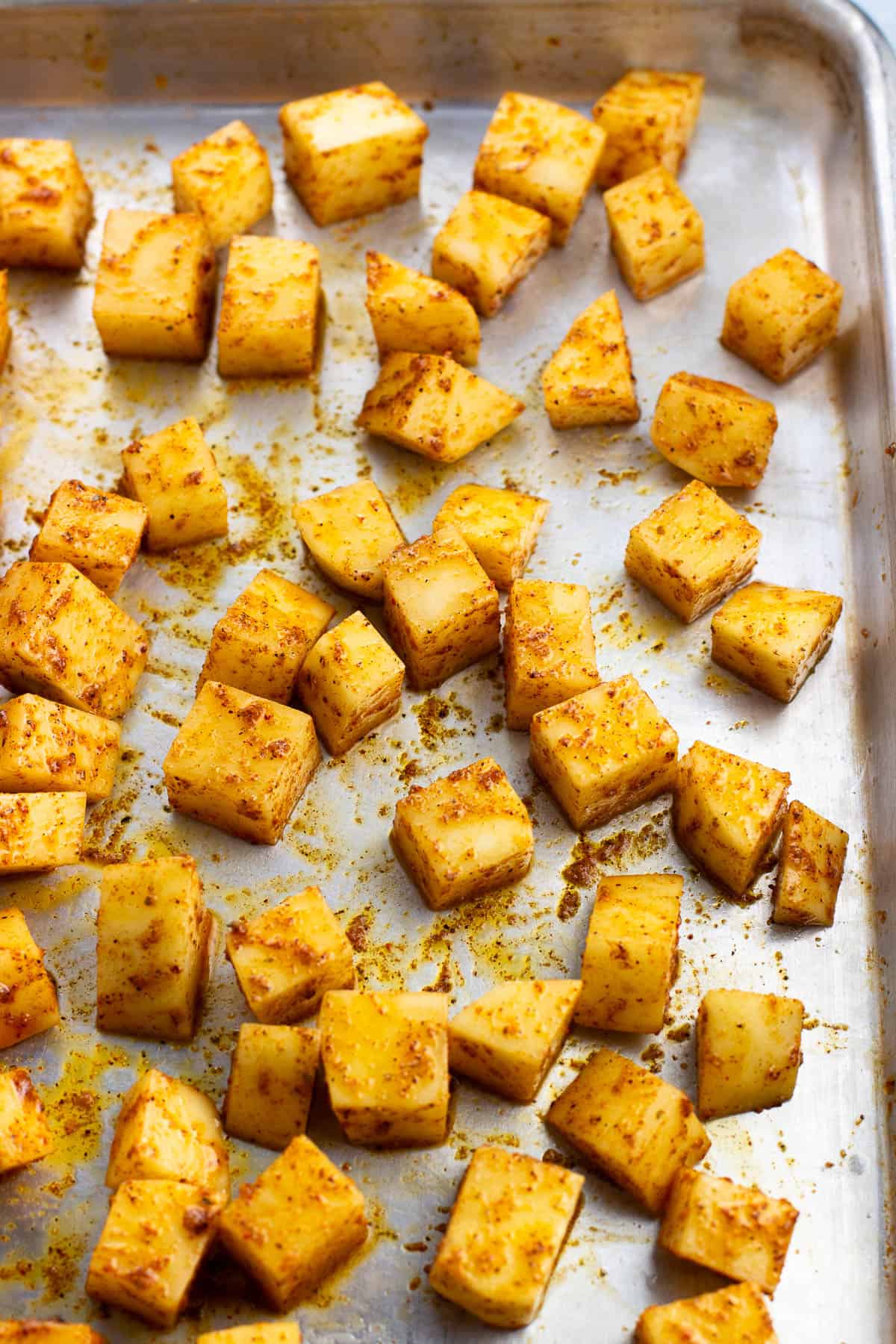 Seasoned potato cubes spread out on a sheet pan.