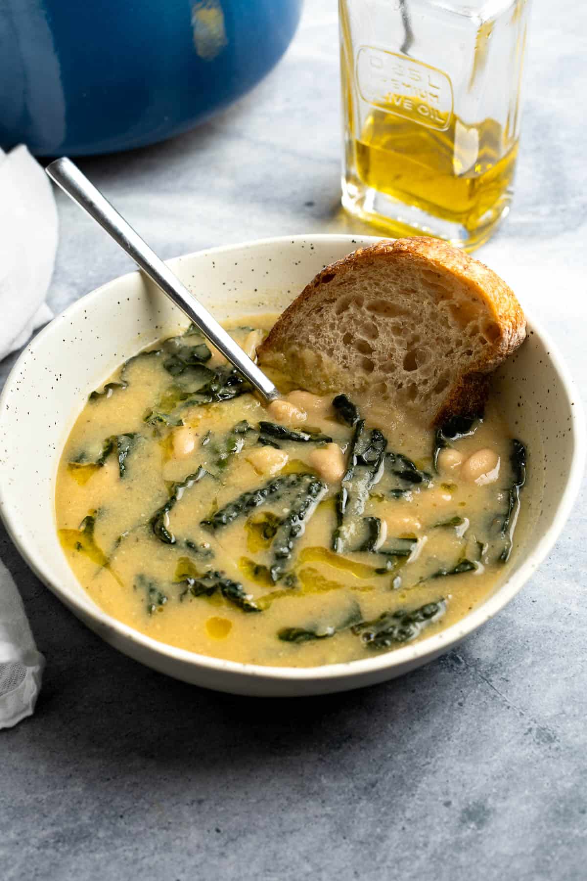 A shallow bowl of potato white bean soup with a side piece of bread.