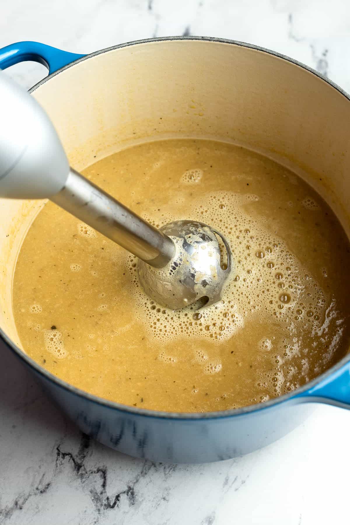 An immersion blender pureeing the soup in the pot.