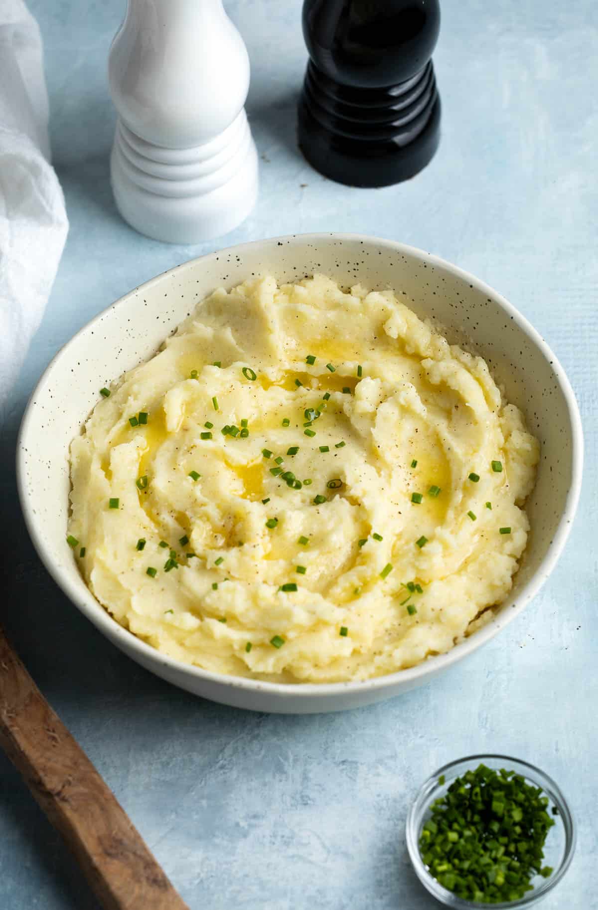 A bowl of mashed potatoes garnished with melted butter and chives.