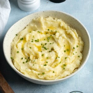 A bowl of mashed potatoes garnished with melted butter and chives.