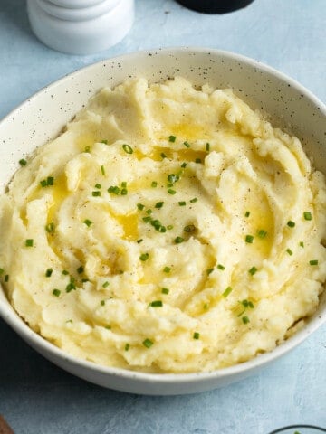 A bowl of mashed potatoes garnished with melted butter and chives.