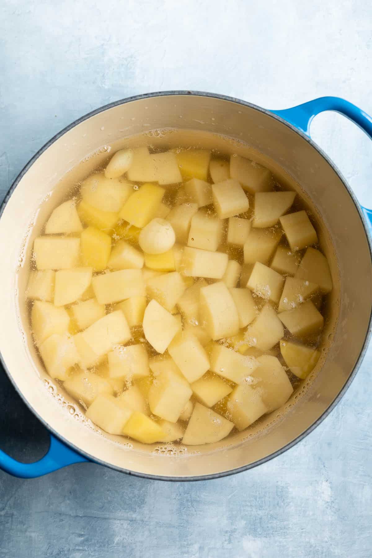 Potato chunks and garlic in a water-filled pot.