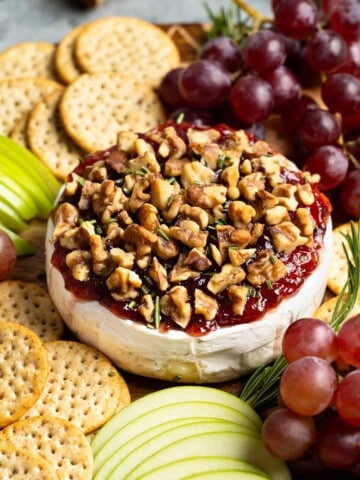 Baked brie topped with jam and walnuts served with apple slices, grapes, and crackers.