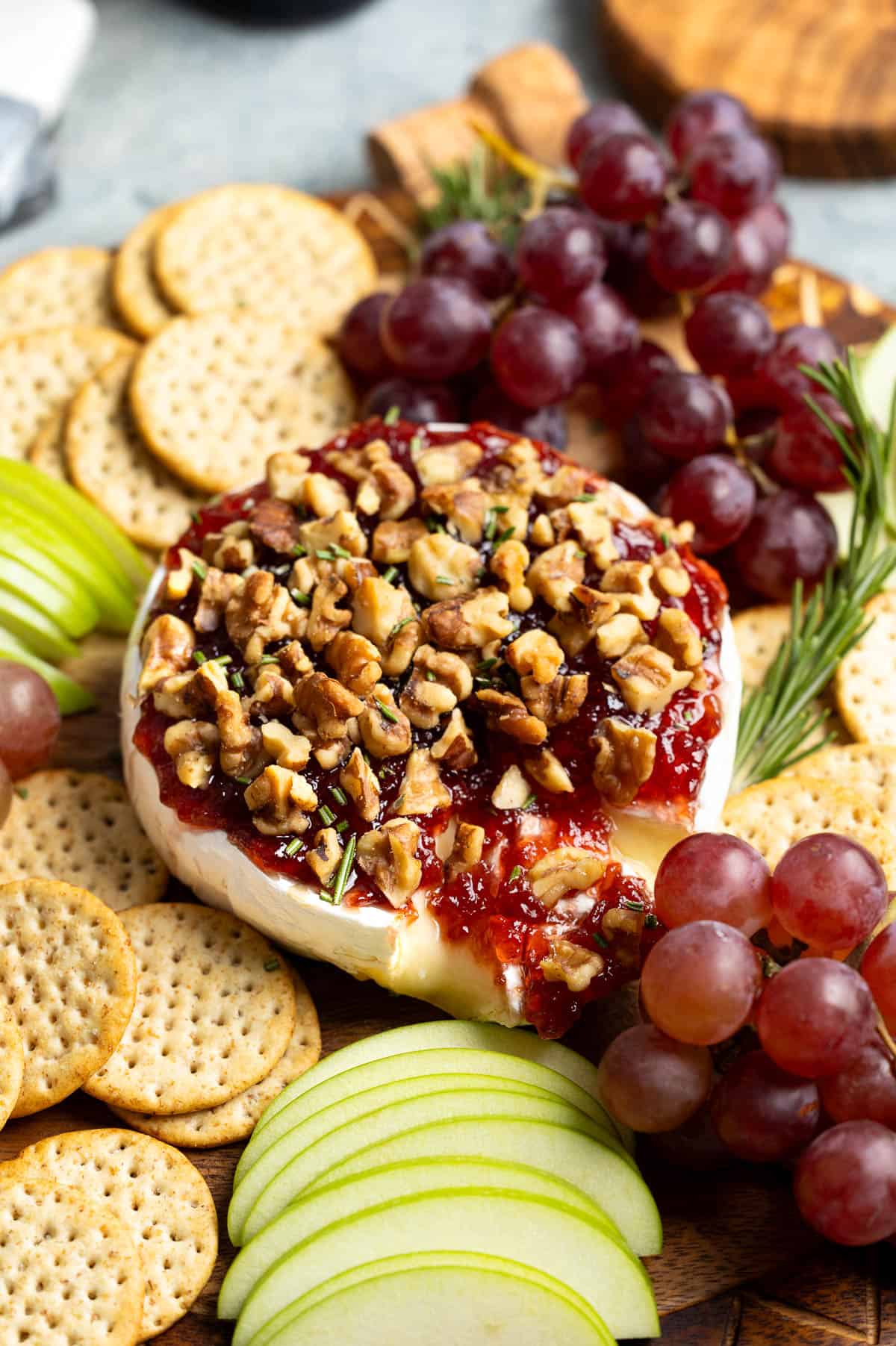 A wheel of gooey baked brie with jam partially cut into on an appetizer board.