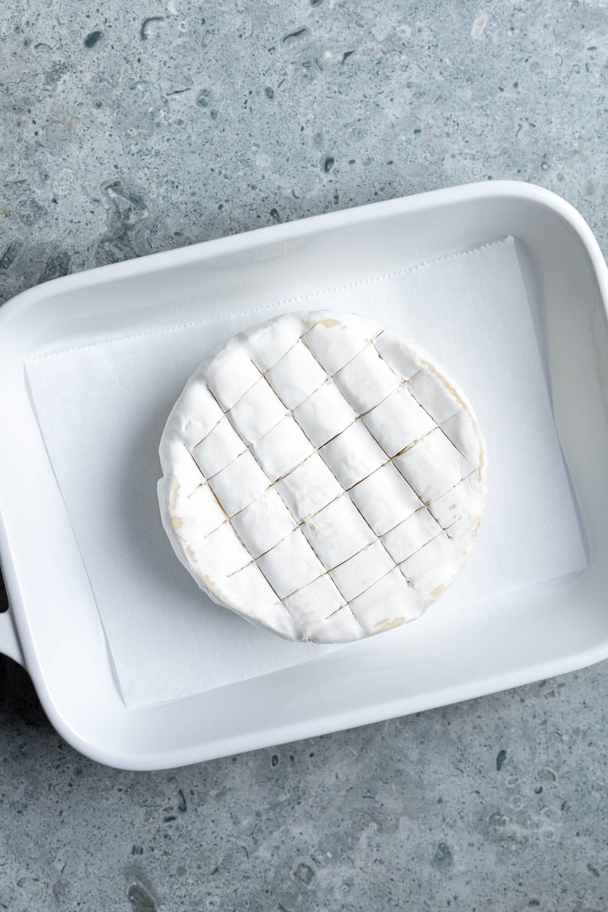 A scored wheel of brie in a parchment-lined baking dish.