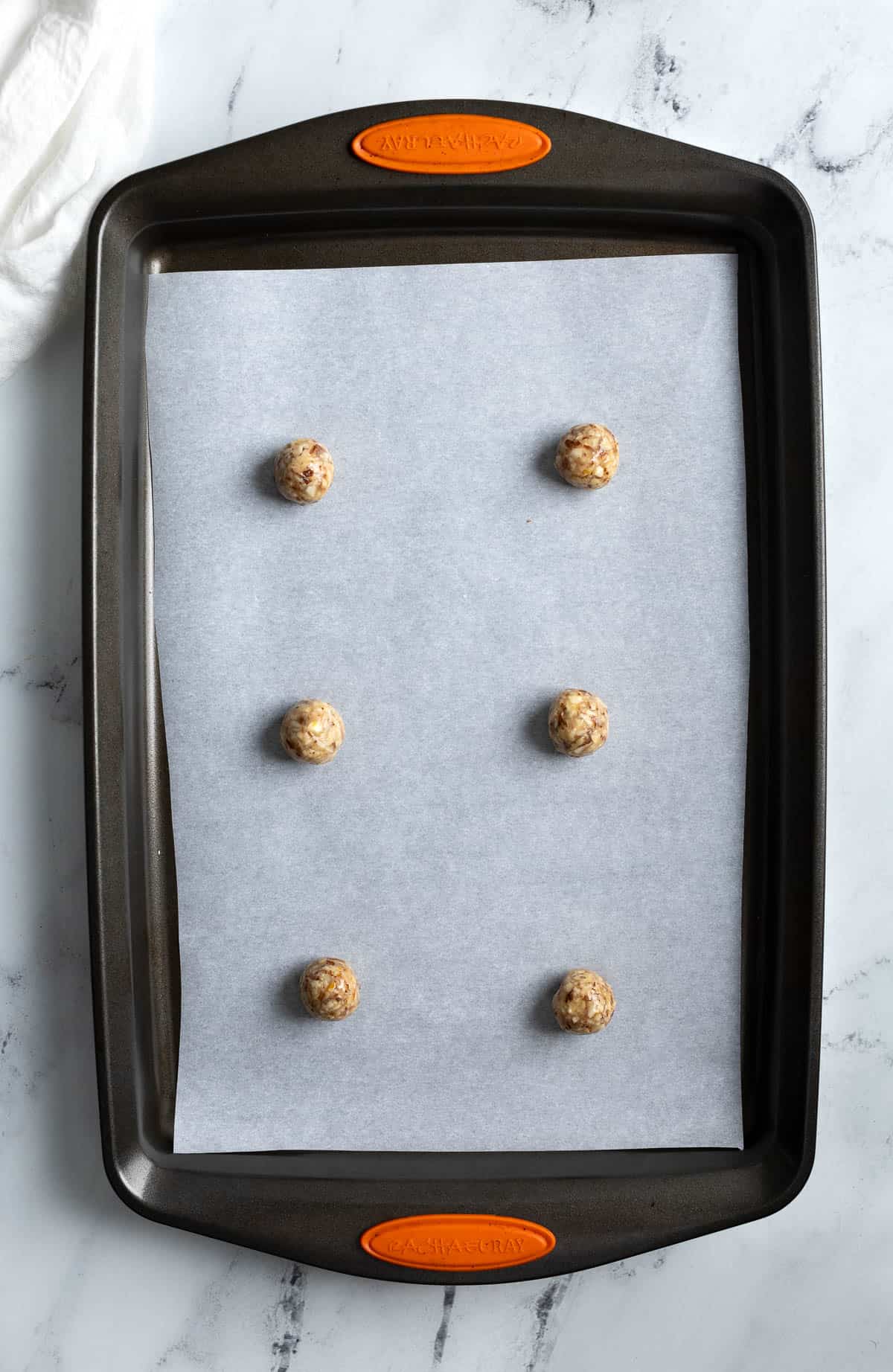 Six cookie dough balls spaced on a parchment-lined baking sheet.