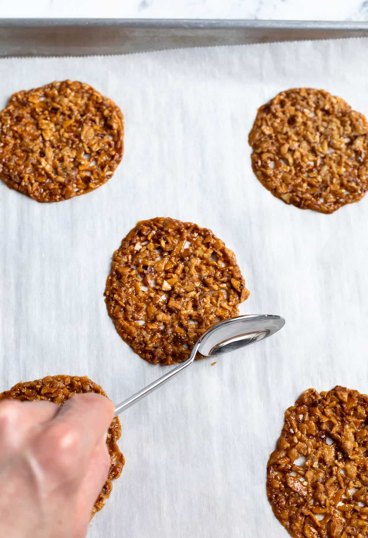 A spoon nudging a cookie into a rounder shape on the pan.