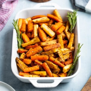 Honey roasted carrots and parsnips in a dish garnished with rosemary sprigs.