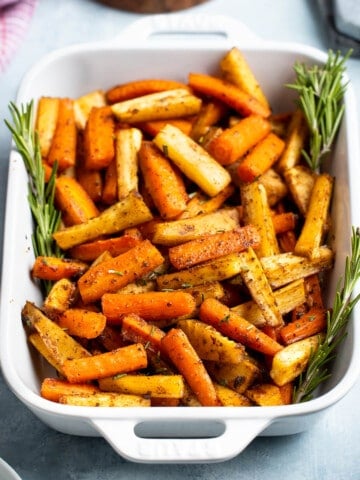 Honey roasted carrots and parsnips in a dish garnished with rosemary sprigs.