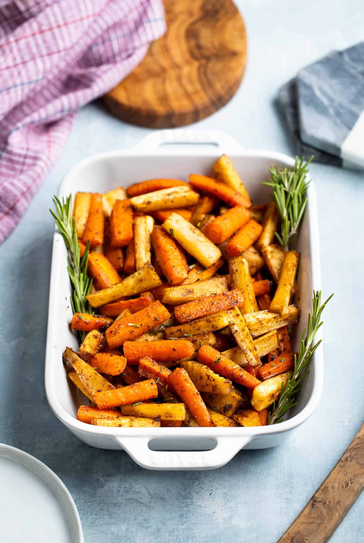 Honey roasted carrots and parsnips in a dish garnished with rosemary sprigs.