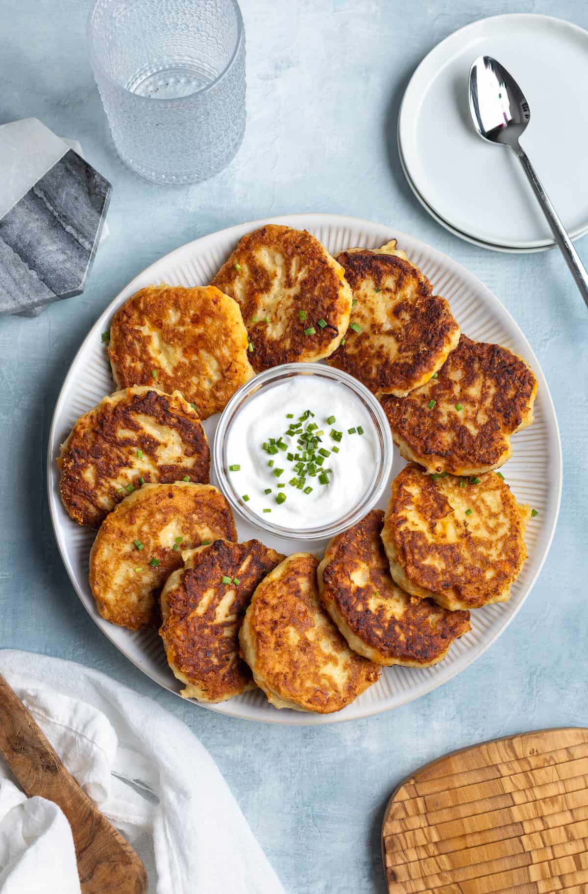 A platter of mashed potato cakes around a bowl of sour cream.