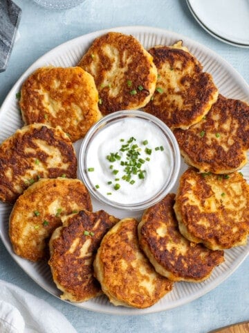A platter of mashed potato cakes around a bowl of sour cream.