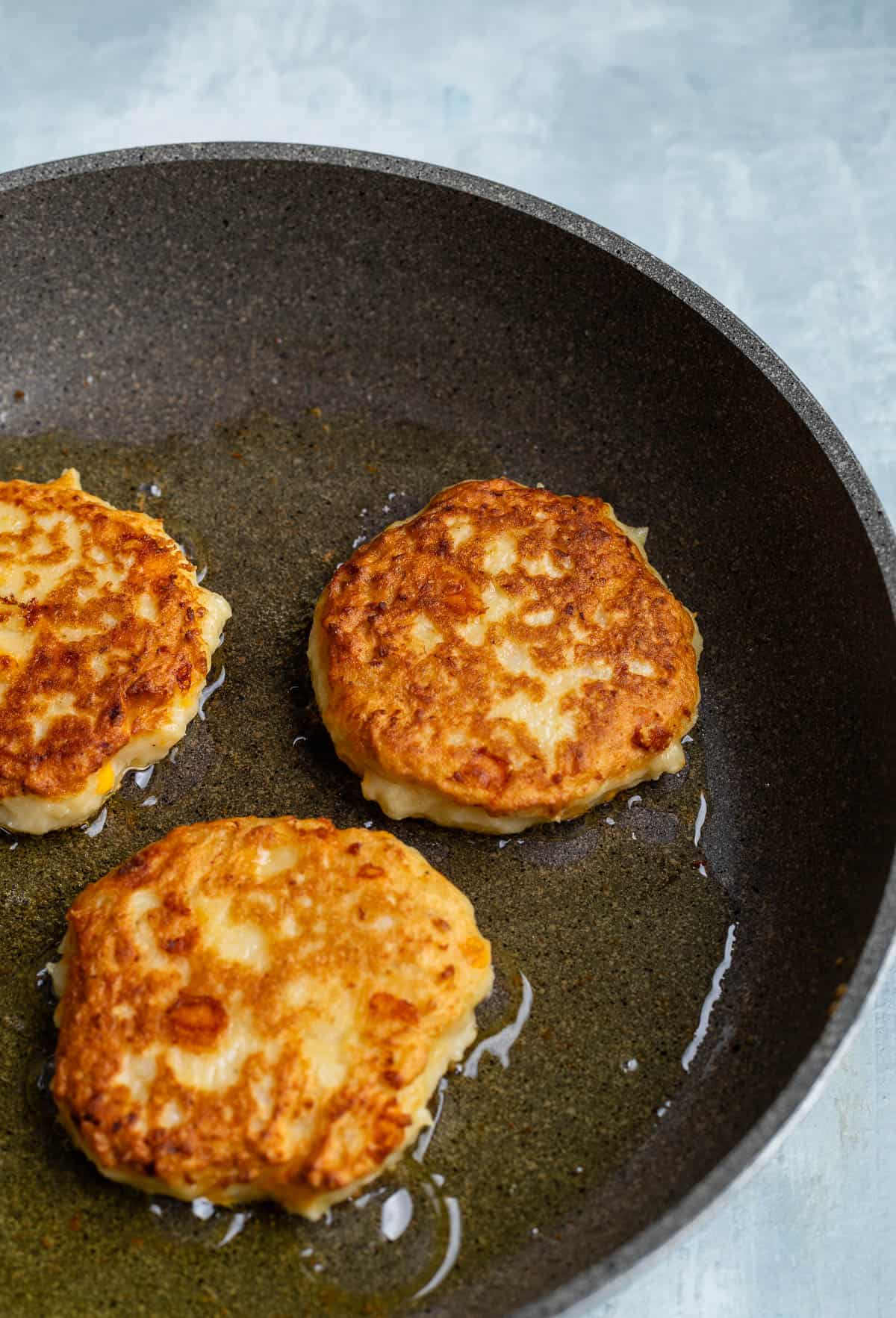 Mashed potato cakes cooking in a pan.