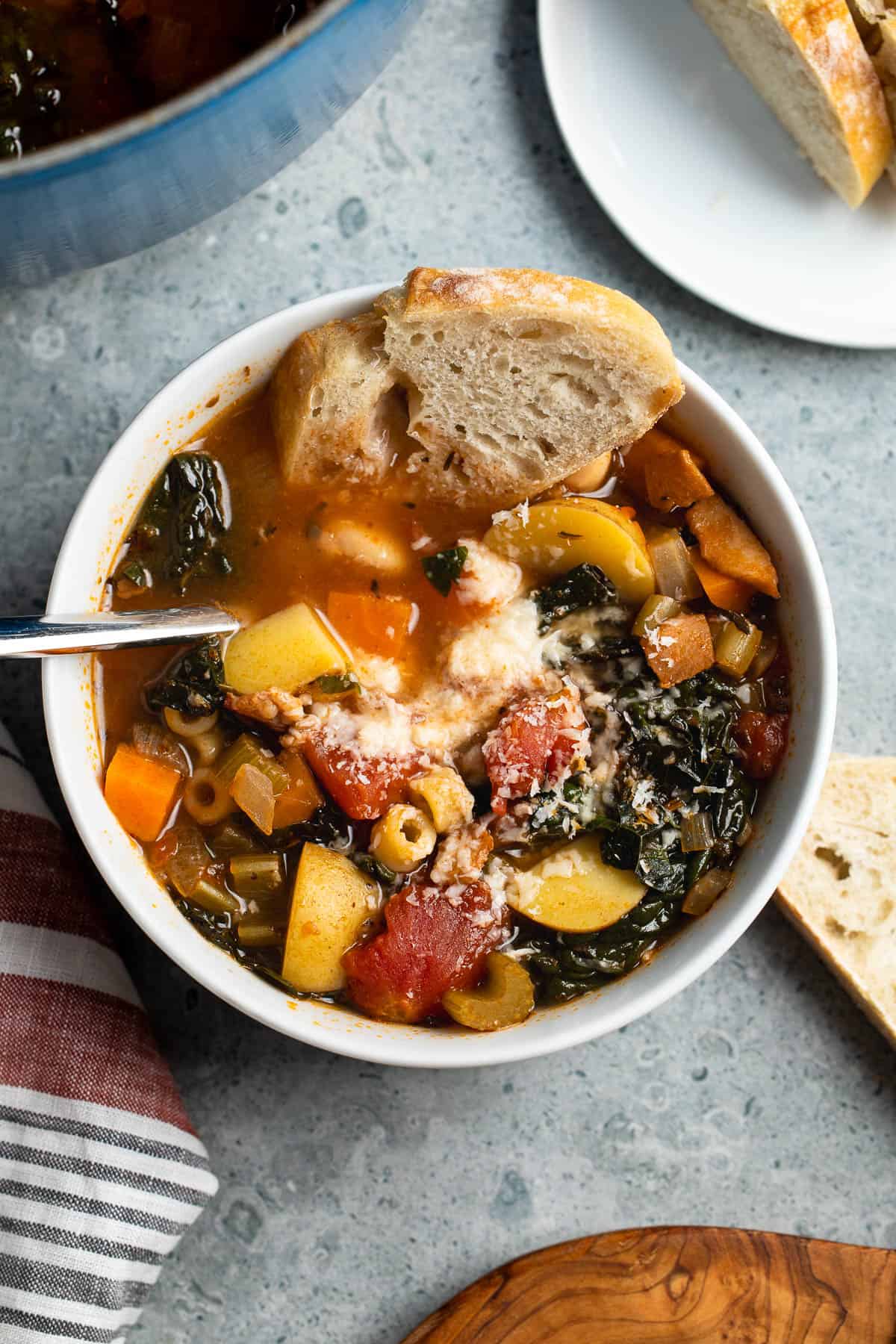 A bowl of minestrone soup with a piece of bread dunked in it.