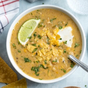 A bowl of white chicken chili topped with sour cream and crushed tortilla chips.