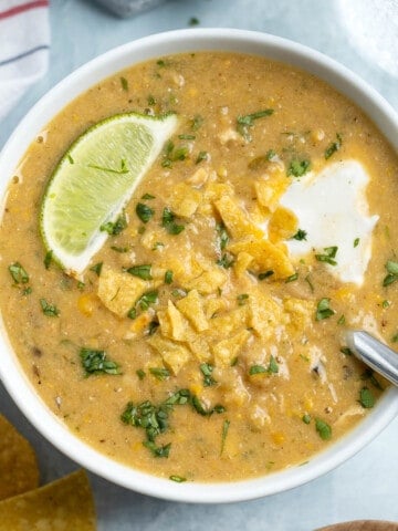 A bowl of white chicken chili topped with sour cream and crushed tortilla chips.