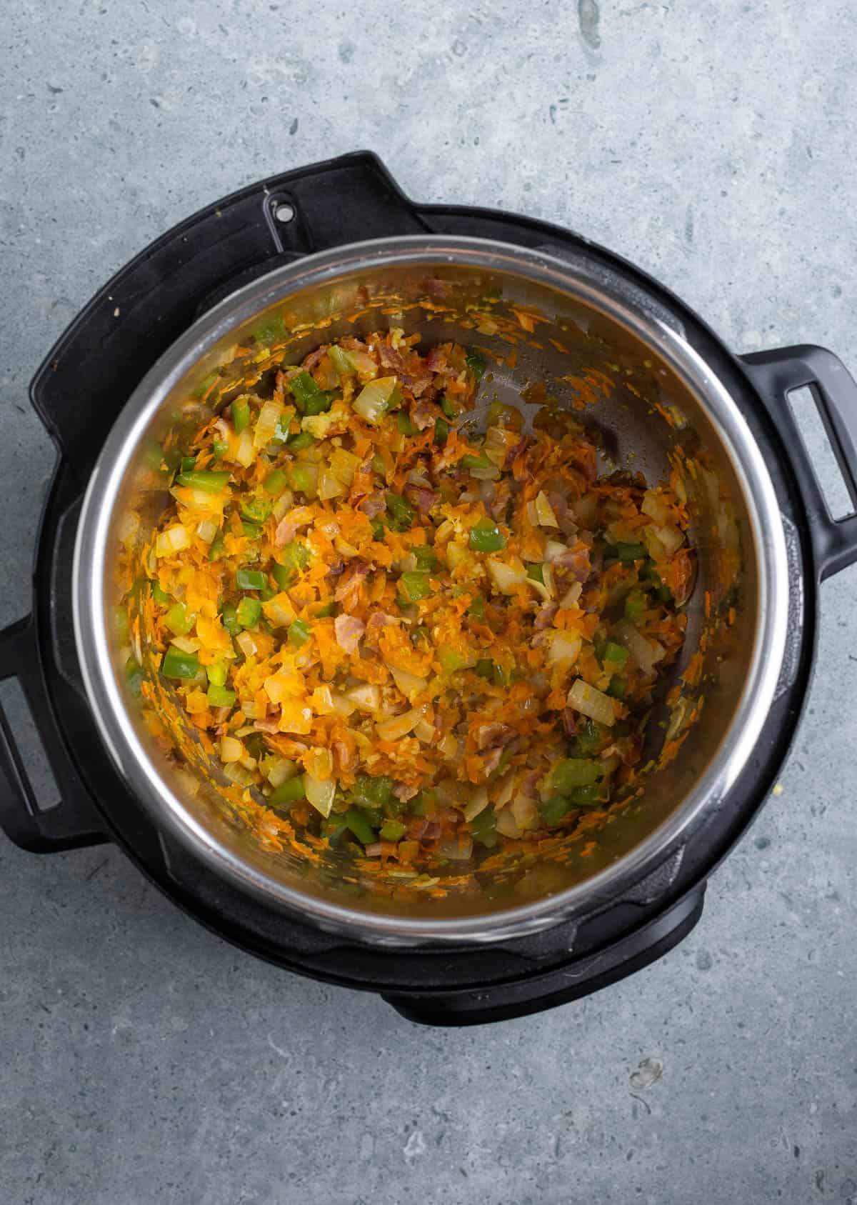 Vegetables, tomato paste, spices, and bacon cooking in the Instant Pot.