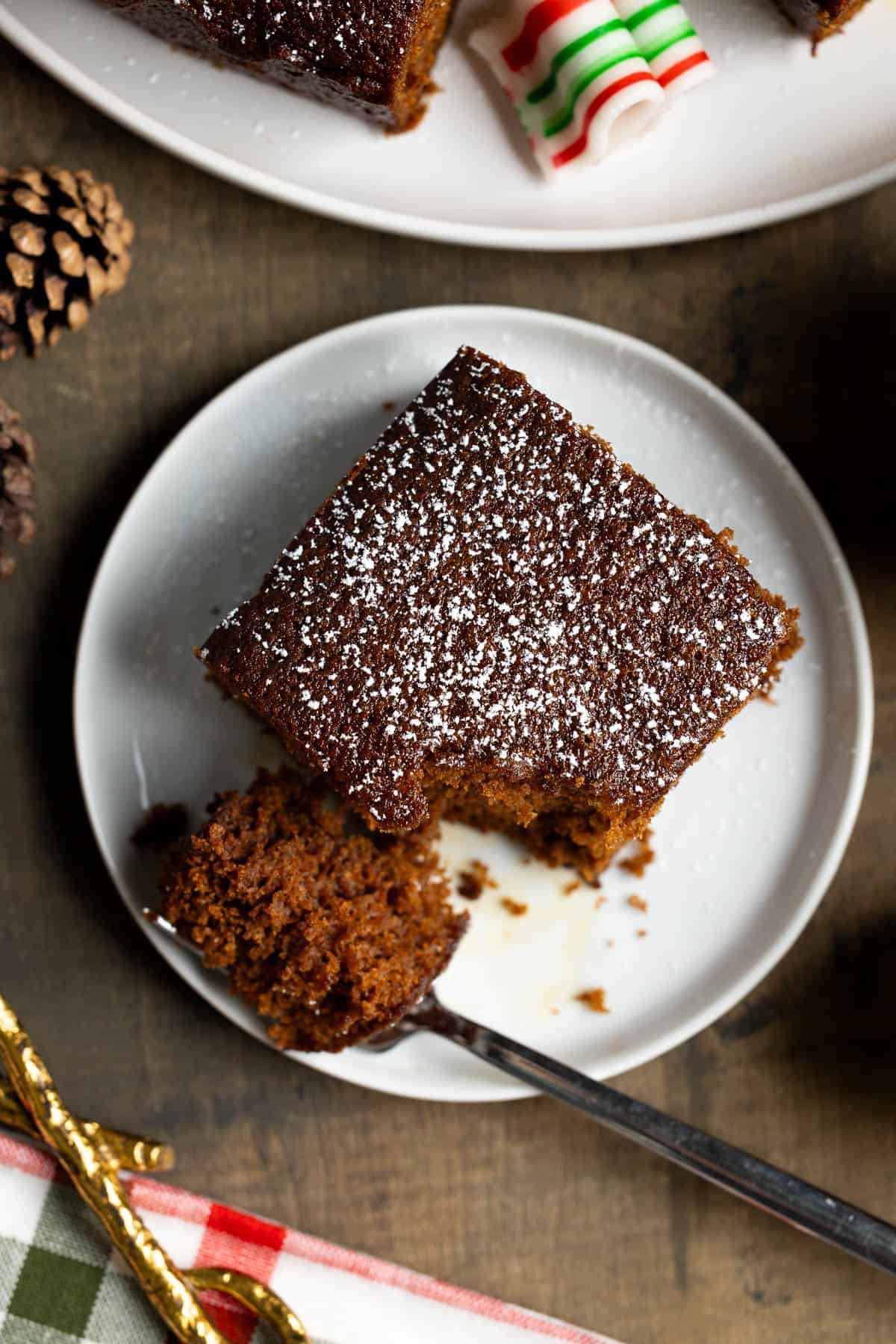 A square of gingerbread cake on a plate with a forkful resting to the side.