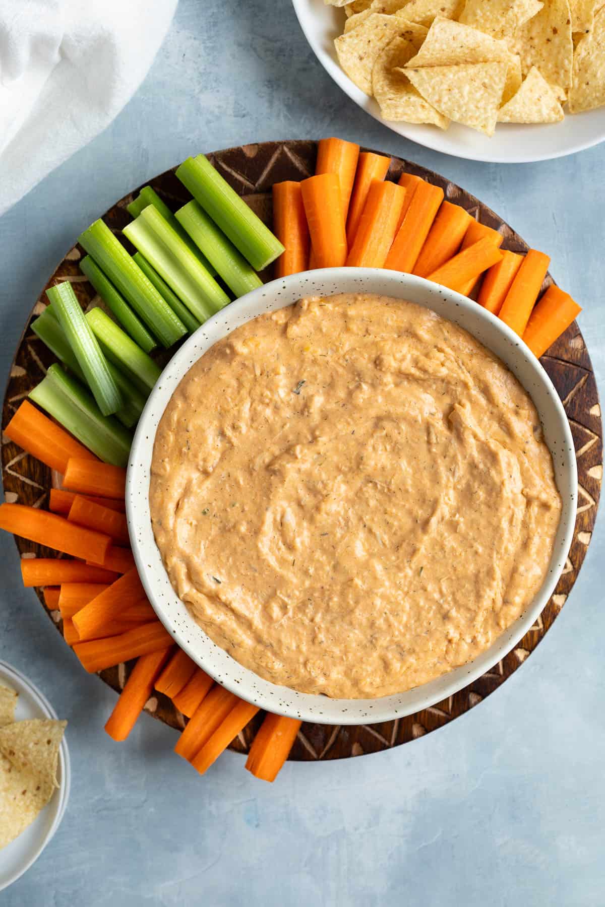 Healthy buffalo chicken dip in a bowl surrounded by carrot and celery sticks.