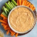 Healthy buffalo chicken dip in a bowl surrounded by carrot and celery sticks.