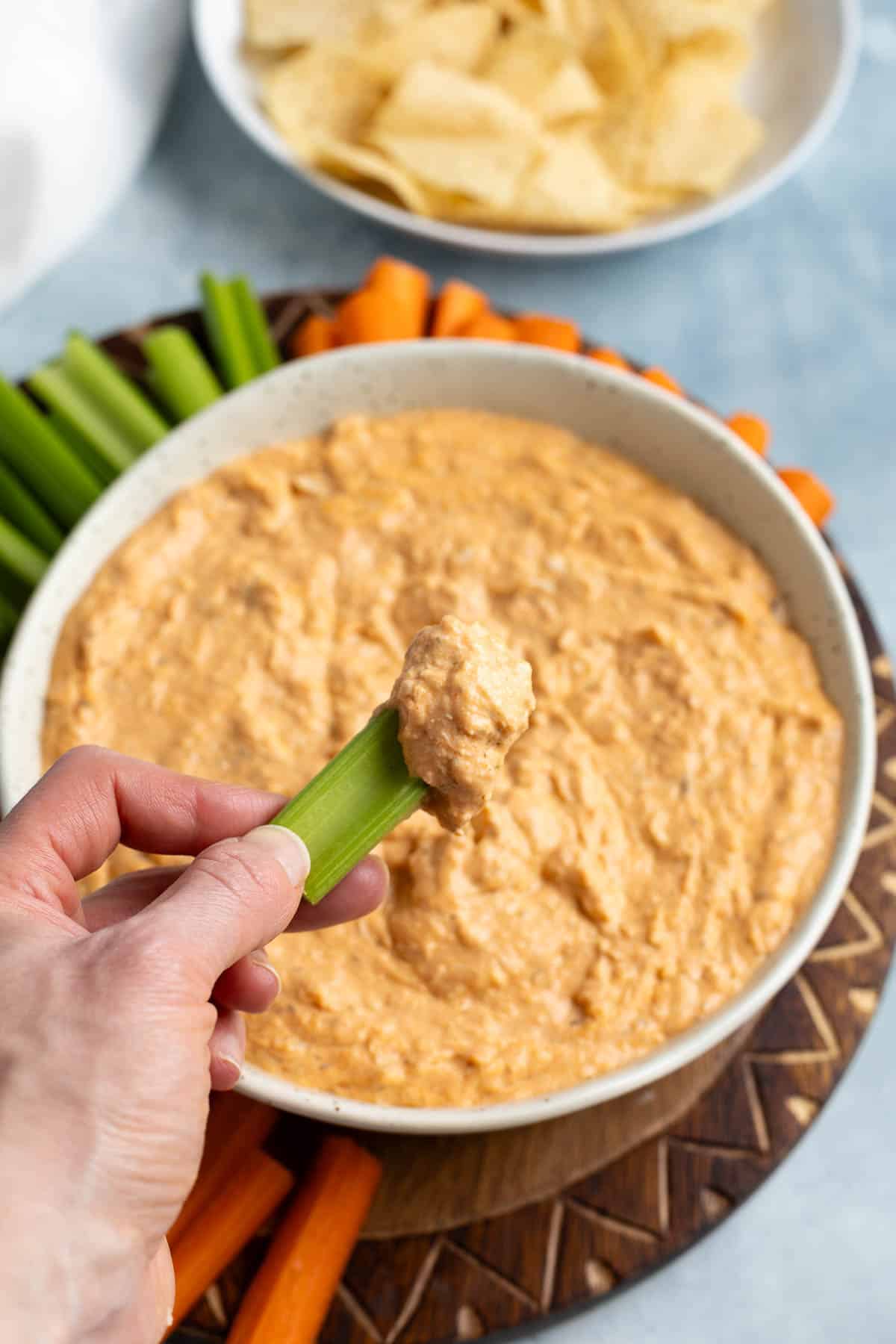A hand holding up a celery stick with a dollop of buffalo chicken dip.