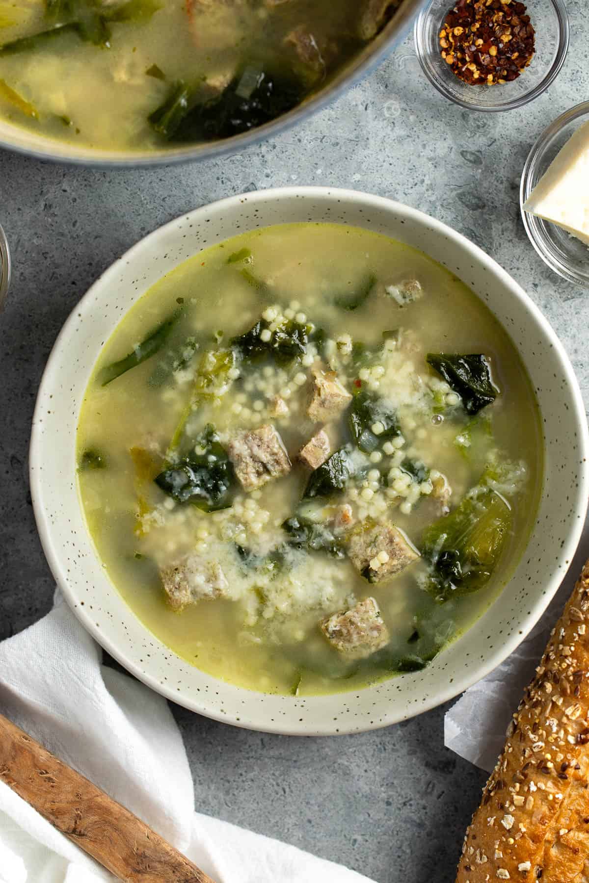 A shallow bowl of Italian wedding soup garnished with grated Pecorino.