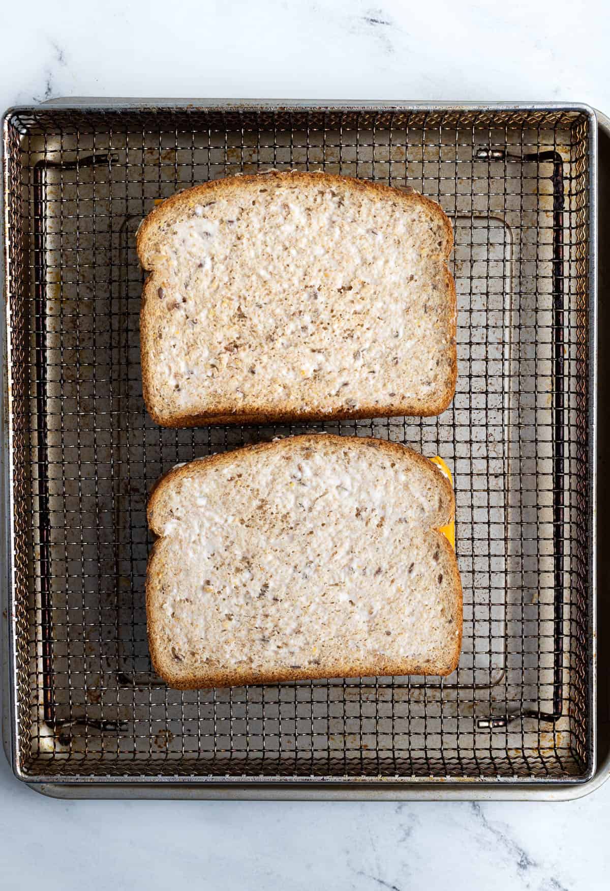 Two grilled cheeses on an air fryer basket before cooking.