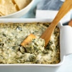 Spinach artichoke dip being scooped out of the serving dish.