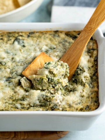 Spinach artichoke dip being scooped out of the serving dish.