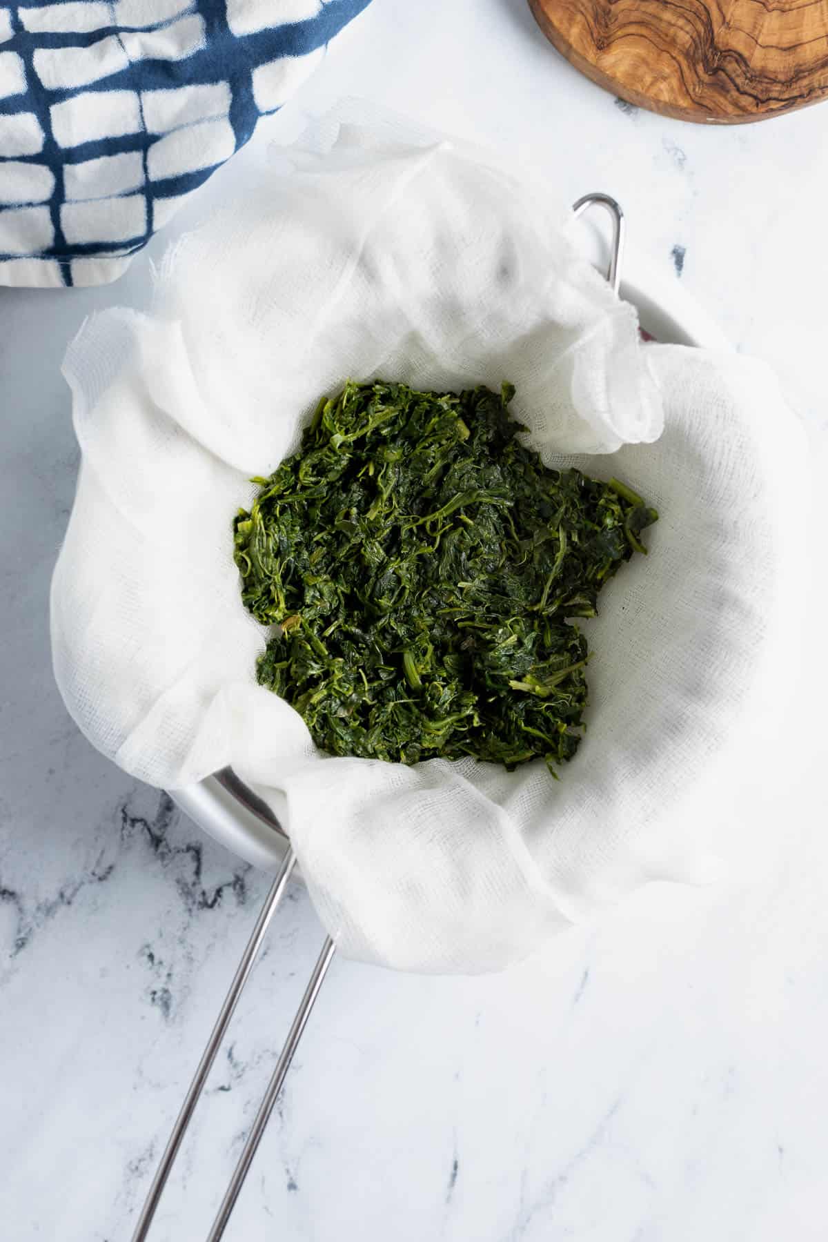 Cooked spinach in a cheesecloth-lined strainer.