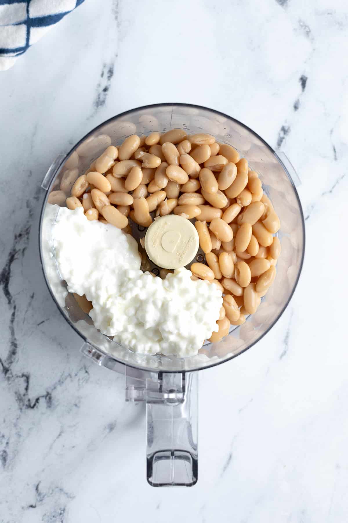 Cannellini beans and cottage cheese in the bowl of a food processor.