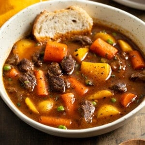 A shallow bowl of Guinness beef stew with a piece of bread dunked in.