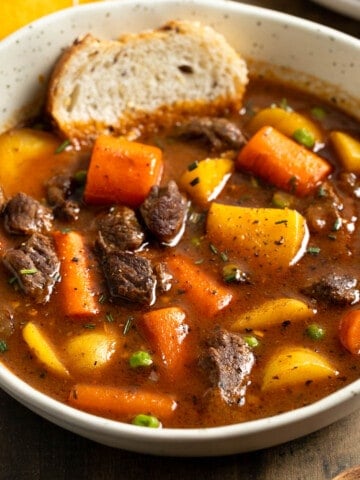 A shallow bowl of Guinness beef stew with a piece of bread dunked in.