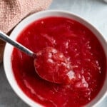 A spoon rising out of a bowl of stewed rhubarb.