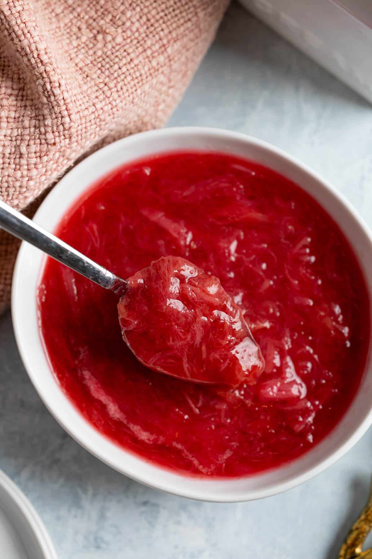 A spoon rising out of a bowl of stewed rhubarb.