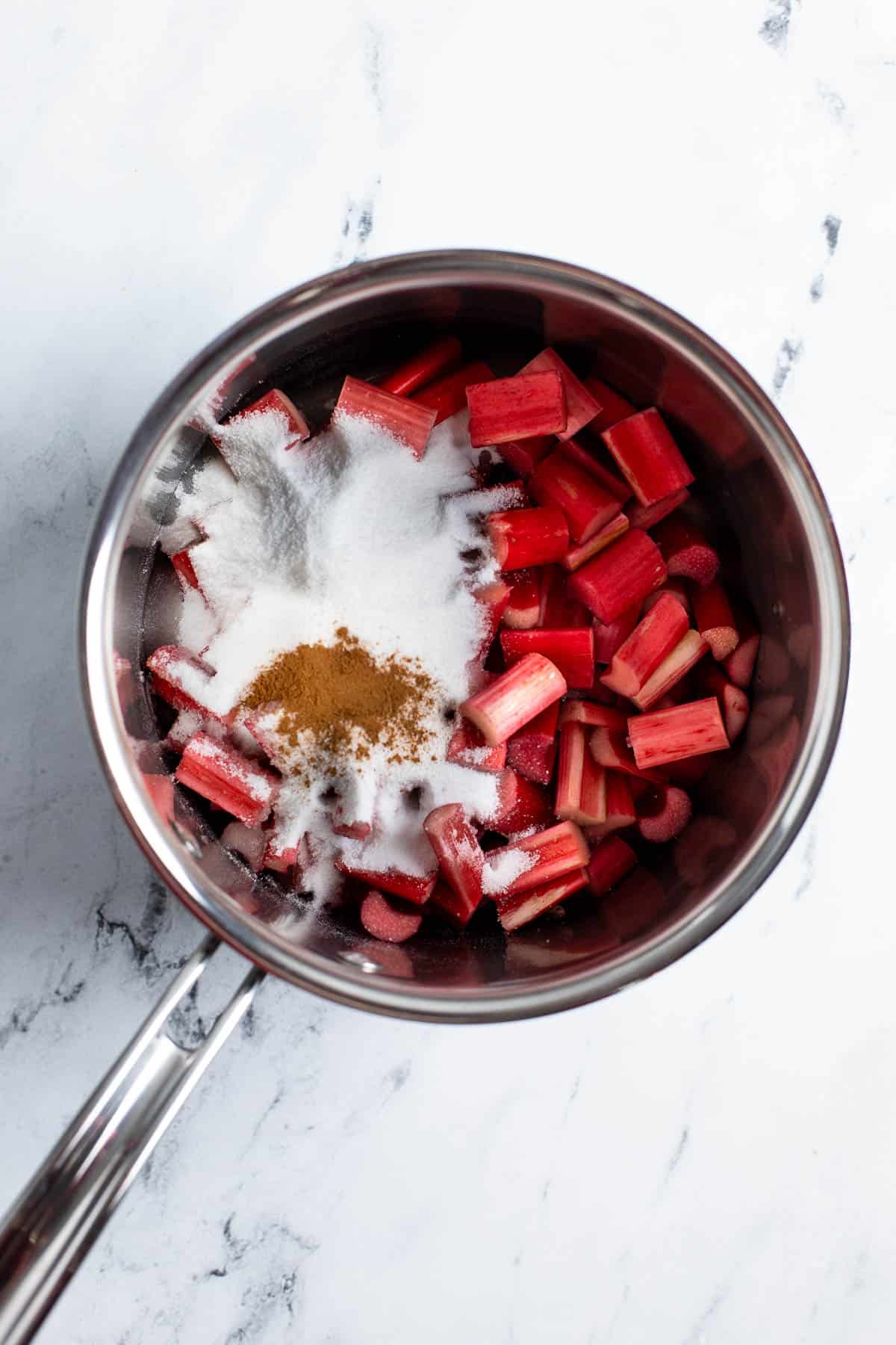 Sliced rhubarb, sugar, water, and cinnamon in a saucepan.