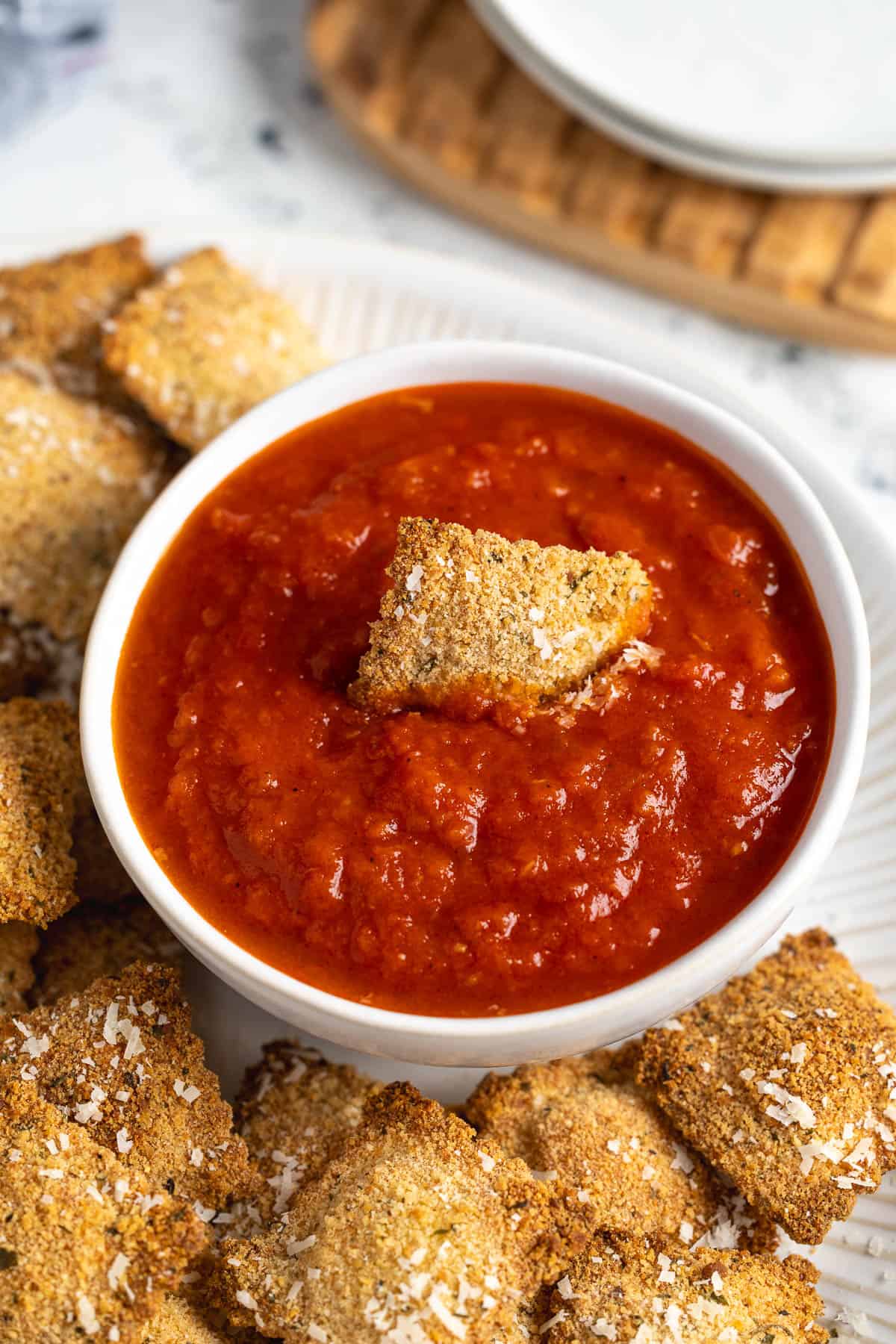 A crispy ravioli being dunked into the bowl of marinara sauce.